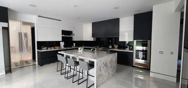 Modern kitchen with black and white lacquered cabinetry, a waterfall marble island and gray bar stools