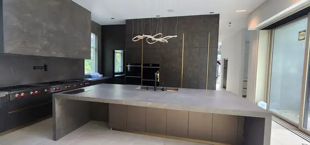 Contemporary kitchen with stone-look slab island, black range wall and sculptural pendant light