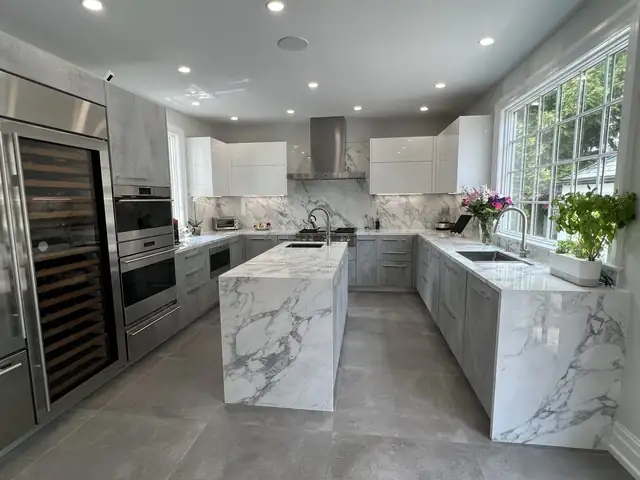 Modern kitchen with twin marble waterfall islands, flat white cabinets and a full-height wine refrigerator
