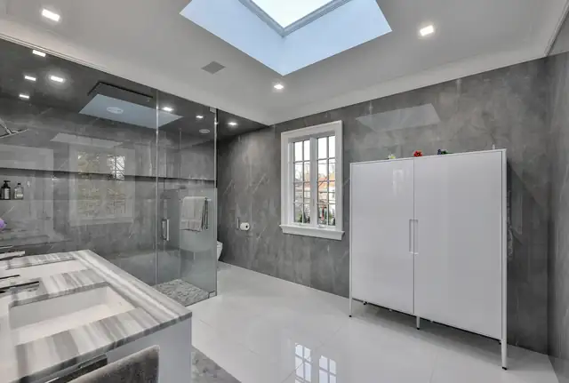 Great Neck, NY master bathroom extension with a skylight, gray porcelain walls, glass shower and white storage tower