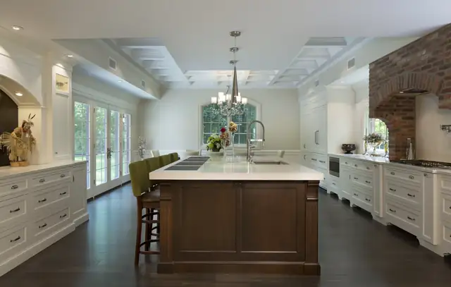 White traditional kitchen by Elite Kitchen & Bath with a stained wood island, brick cooking hearth, coffered ceiling and lantern pendants