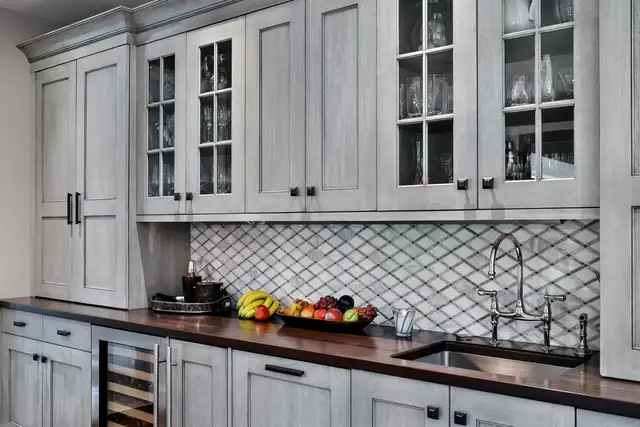 Glen Head entertainment bar with gray glazed cabinets, glass uppers, wood counter and wine refrigerator